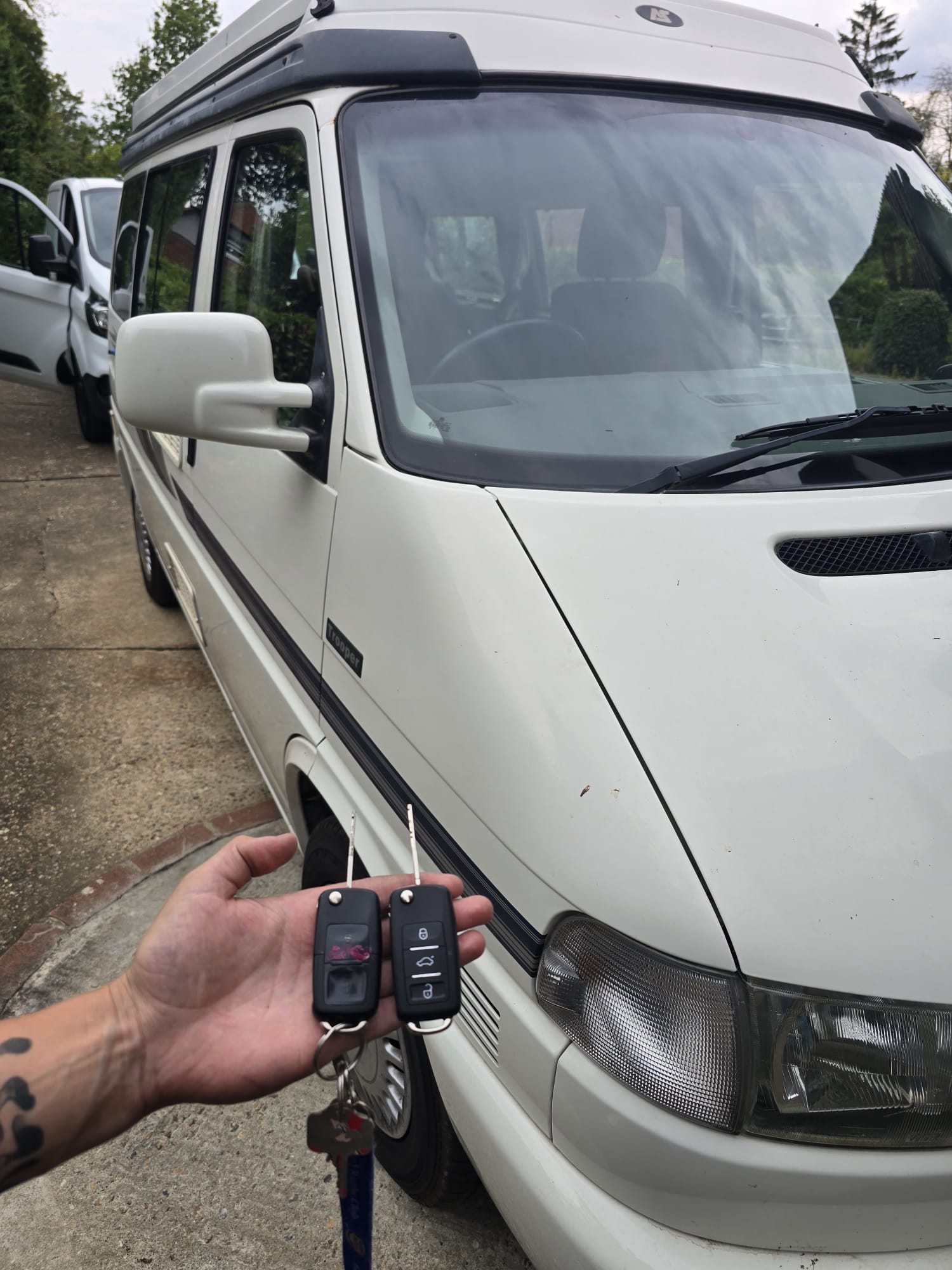 Two replacement remote keys held beside a white VW T4 campervan