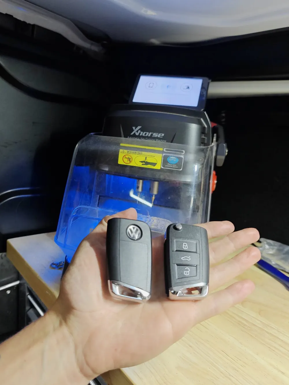 Two VW flip keys held in front of an Xhorse key cutting machine in the van