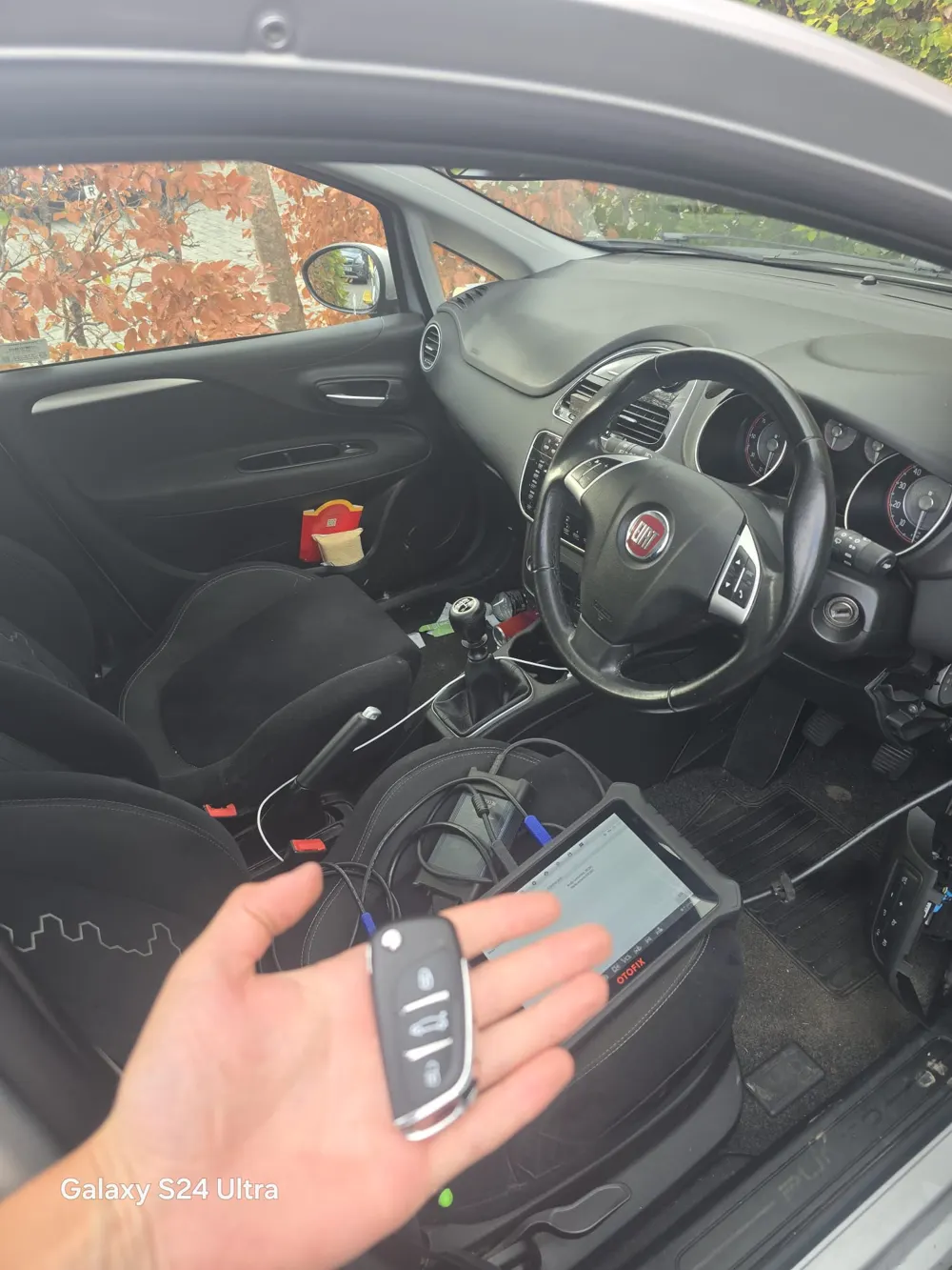 Replacement flip key held inside a Fiat Punto with a diagnostic tablet on the seat
