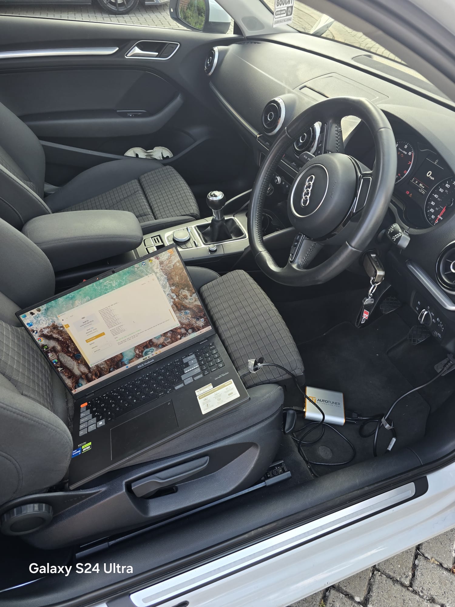 White Audi A3 interior with laptop and AutoTuner device mid ECU read and remap session on the driver seat