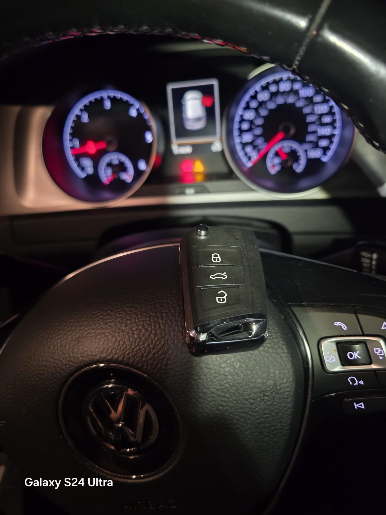 VW replacement flip key resting on the steering wheel with the instrument cluster lit after programming