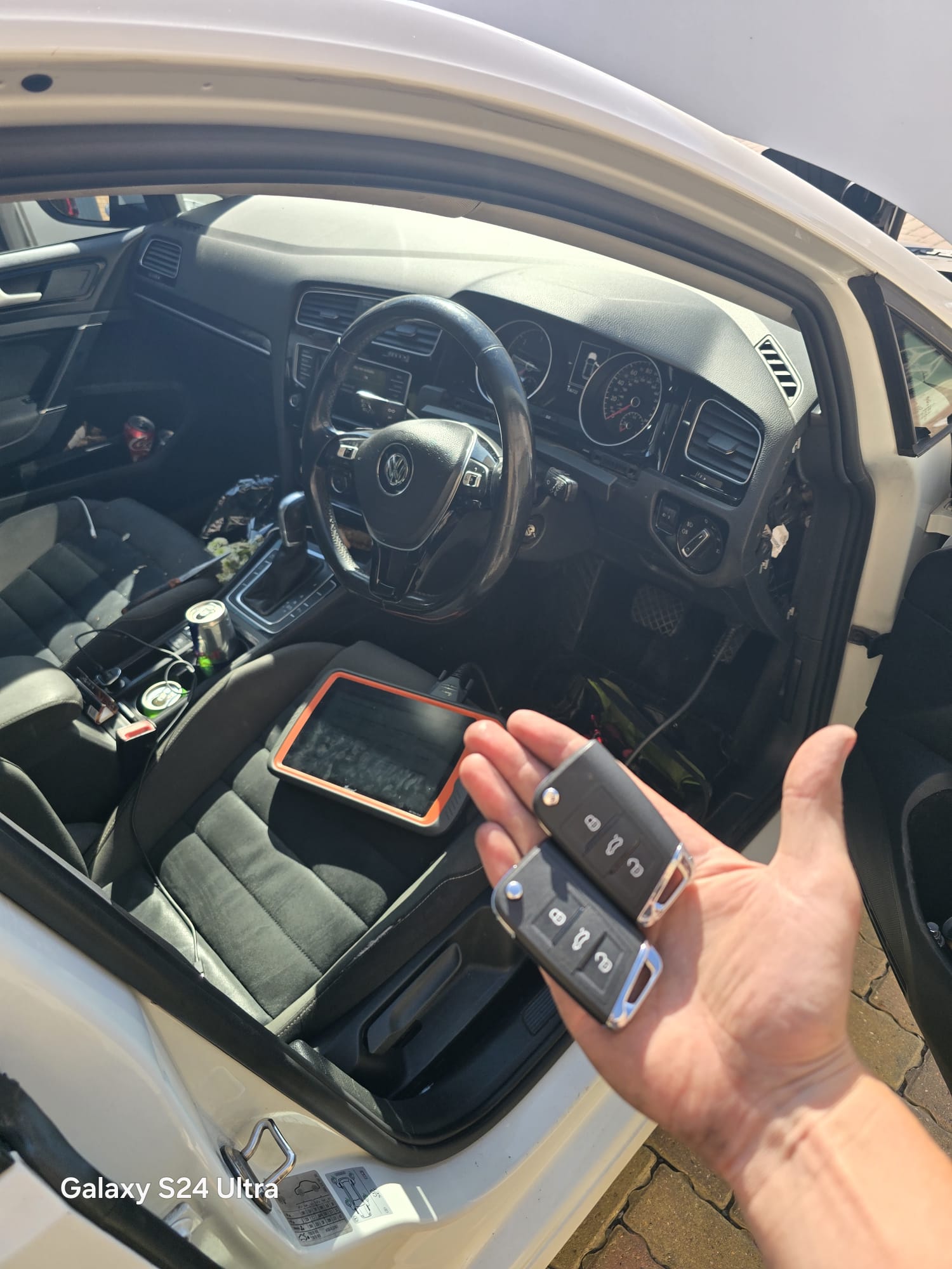 Pair of newly programmed VW Golf remote flip keys held beside the open driver door with diagnostic tablet inside