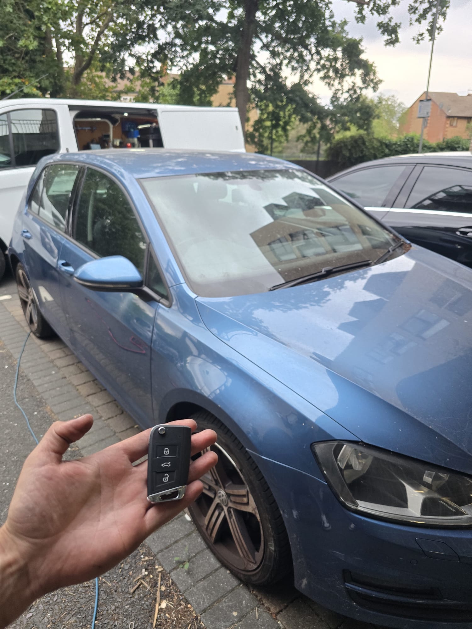 Newly cut VW Golf flip key held in front of a blue Golf during a mobile locksmith job