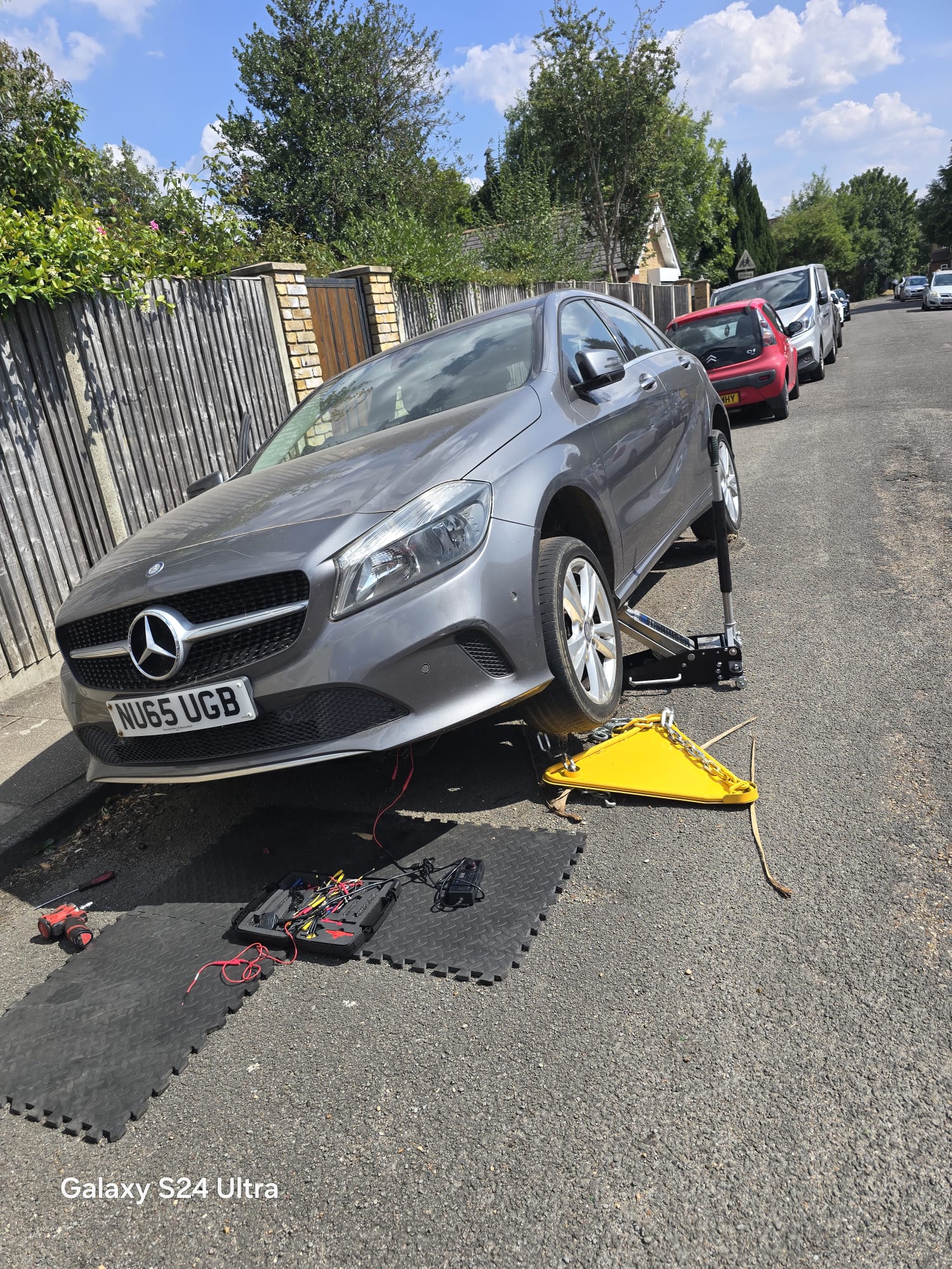 Mercedes A-Class jacked up on a residential street with mobile diagnostic and wiring tools laid out for an on-site electrical repair