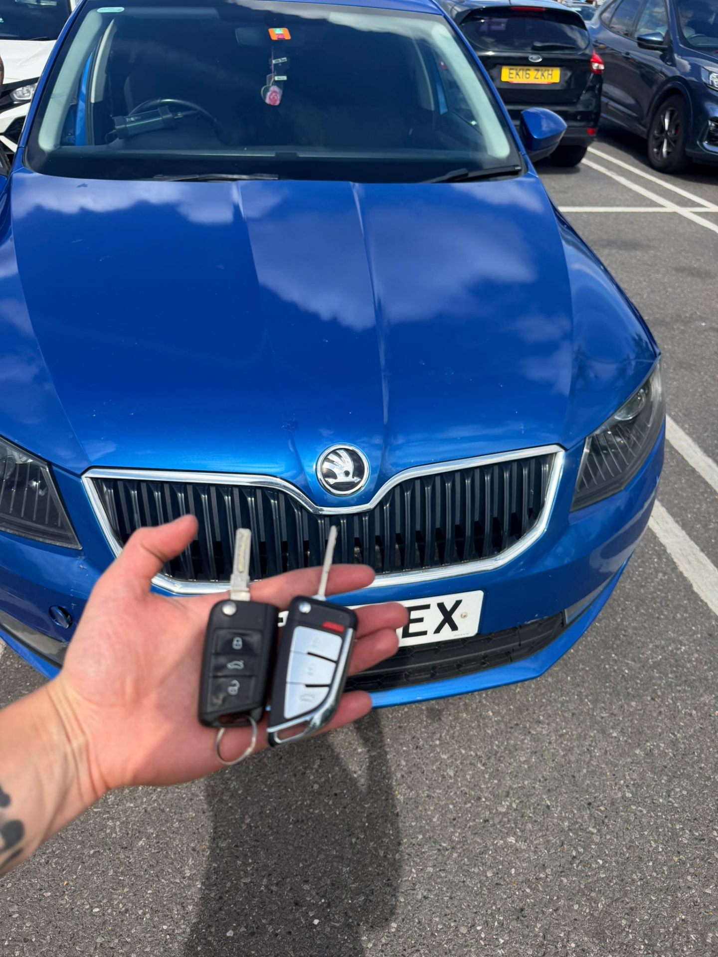Pair of Skoda Superb keys programmed in front of a blue Skoda Superb
