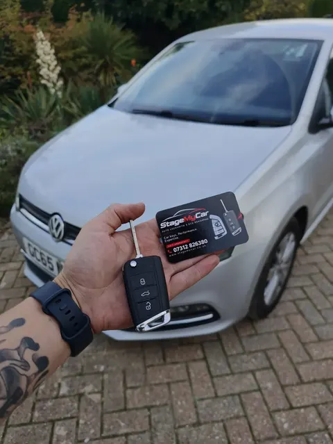 Replacement VW flip key and StageMyCar business card in front of a silver VW Polo